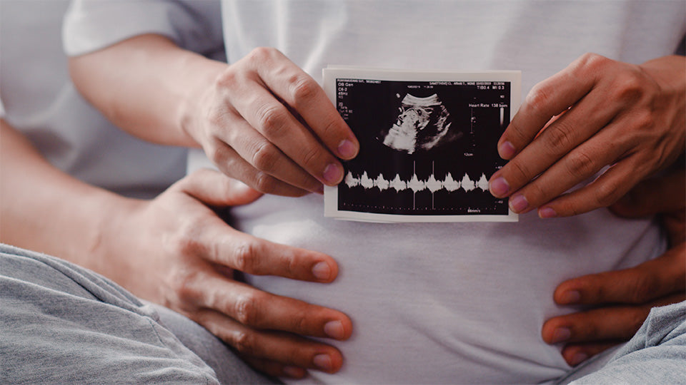 young asian pregnant couple show looking ultrasound photo baby belly mom dad feeling happy smiling peaceful while take care child lying sofa living room home