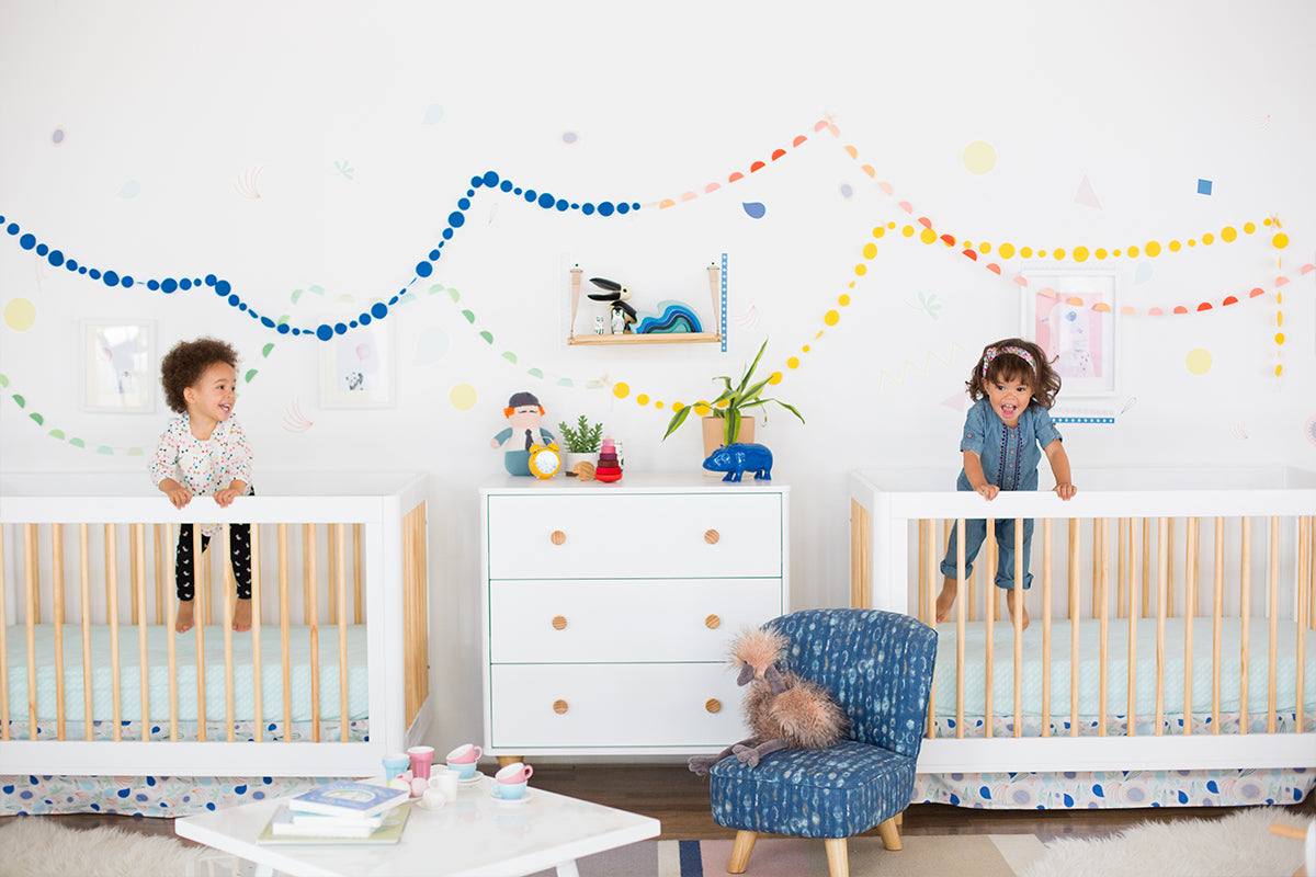 two babies inside babyletto lolly white and natural cribs laughing