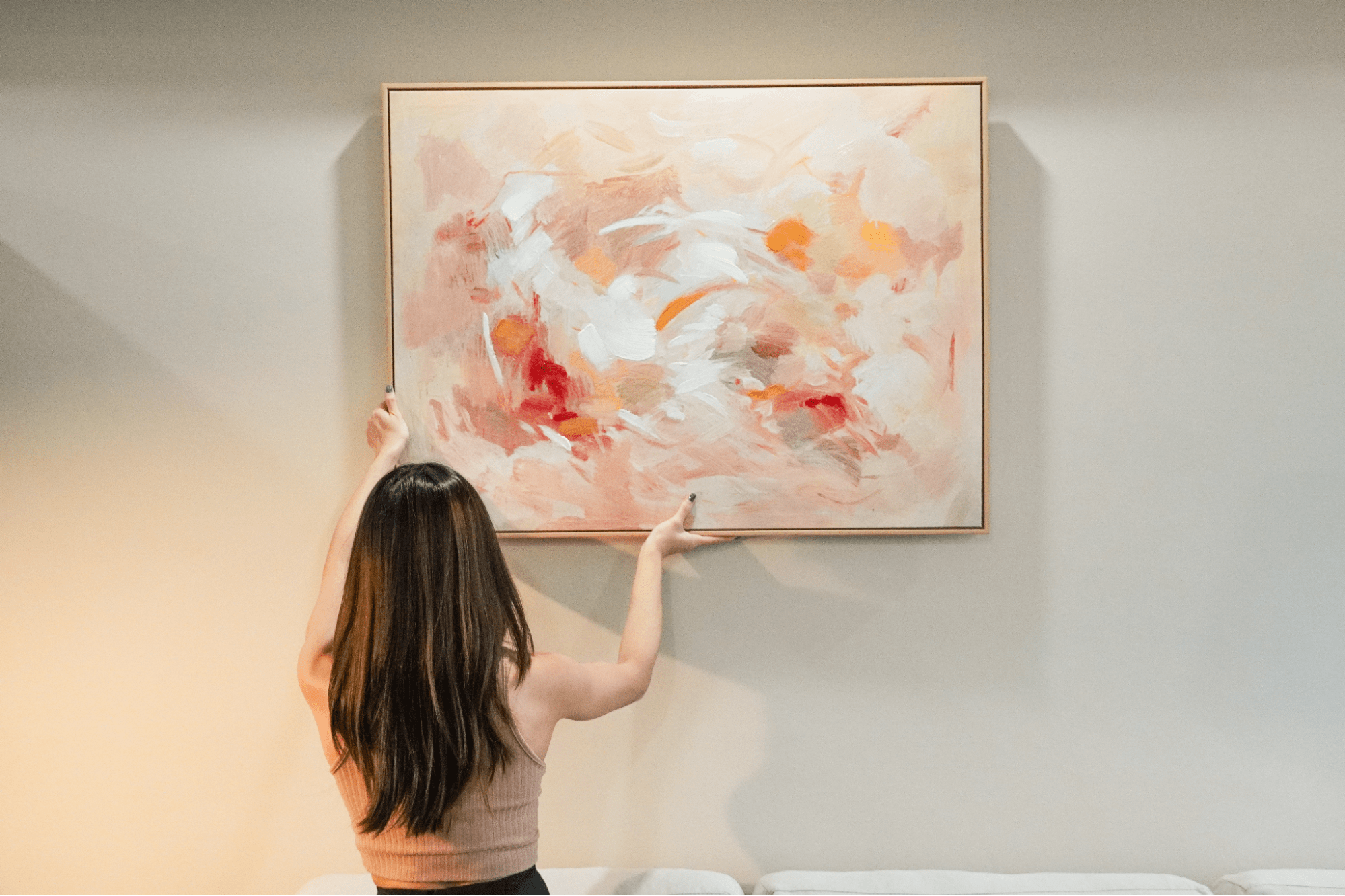 Lady hanging up a piece of wall art on a blank wall