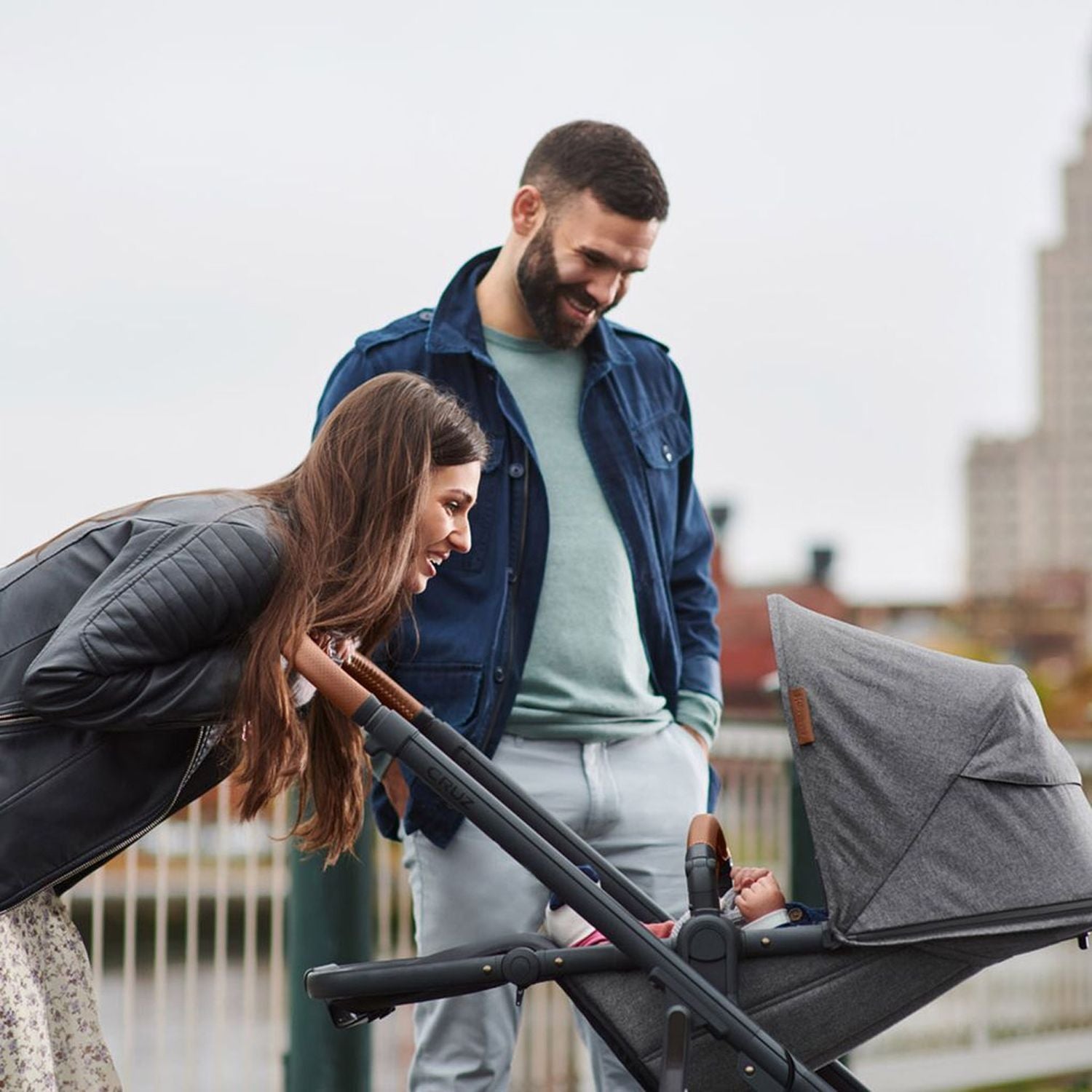 Parents smiling at their baby inside the Uppababy Cruz 2 Greyson Reversible Stroller#color_greyson