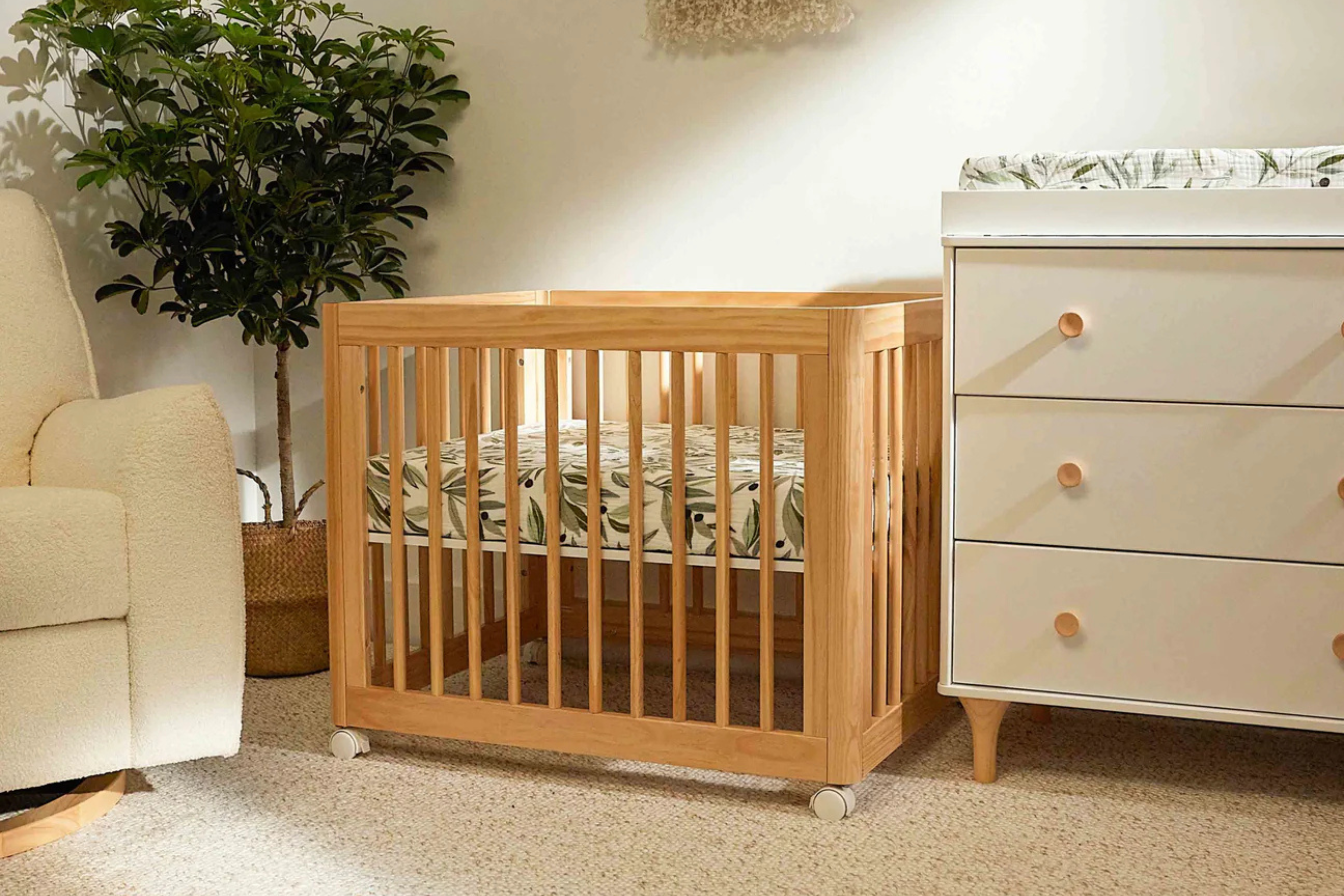 Babyletto Yuzu 8-in-1 Convertible Crib Natural in midi configuration placed inbetween a nursing chair and dresser#color_natural